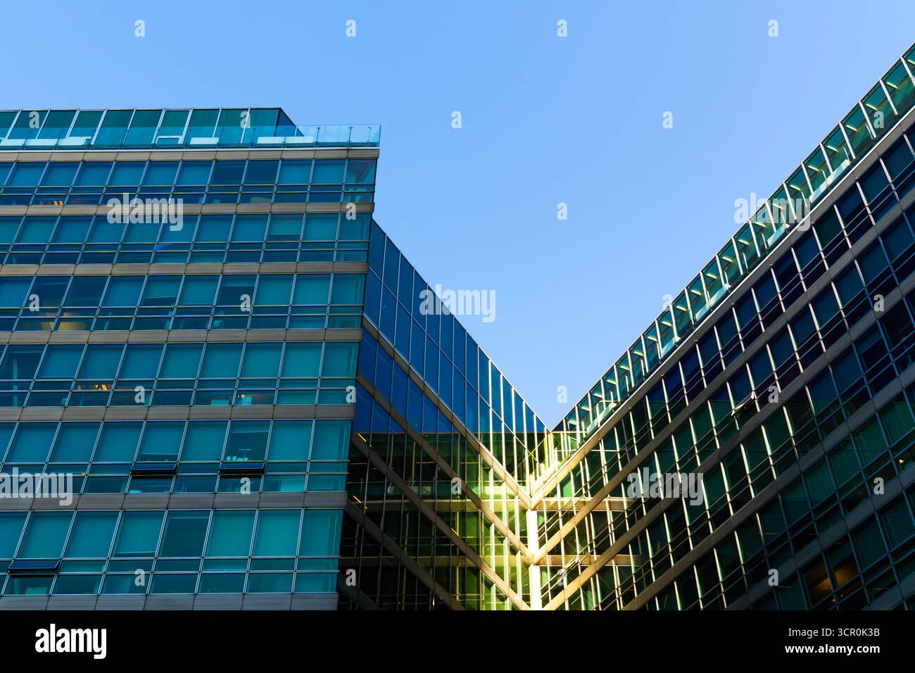 Edificio contemporaneo per uffici con facciata metallica e design geometrico in vetro sotto un cielo blu chiaro e profondo Foto Stock