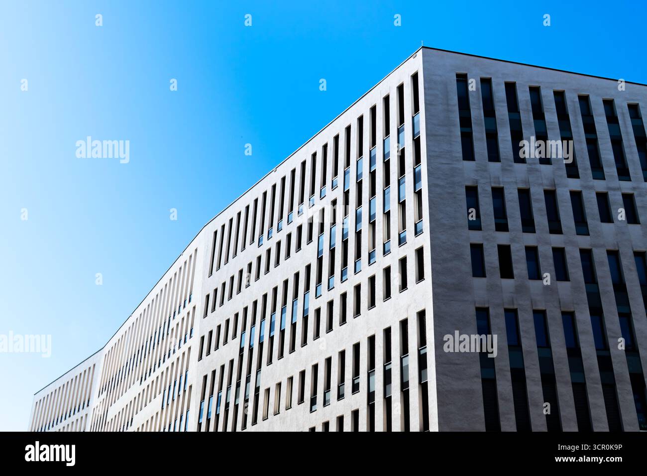 Edificio di uffici contemporaneo con finestre verticali e facciata bianca pulita sotto un cielo blu chiaro Foto Stock