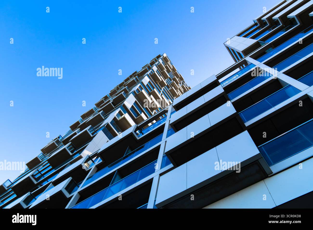 Moderno edificio residenziale con finestre a bovindo geometriche e vetro blu riflettente che creano una struttura architettonica dinamica Foto Stock