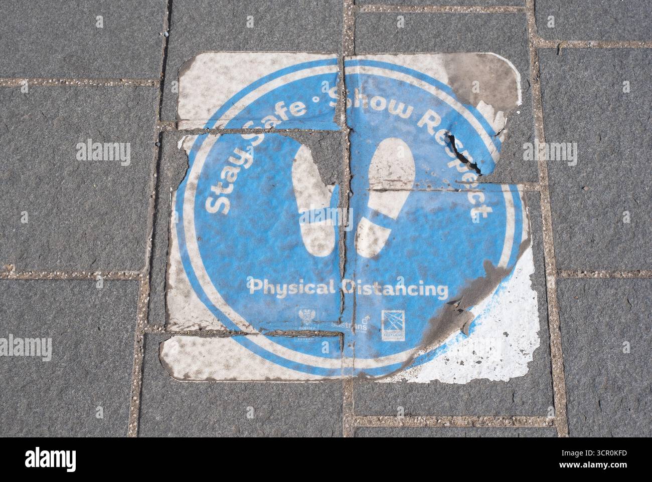 Segnaletica sul marciapiede che fa riferimento alle norme di distanziamento sociale durante la pandemia di covid. Aberfeldy, Perth e Kinross, Scozia, settembre 2025. Foto Stock