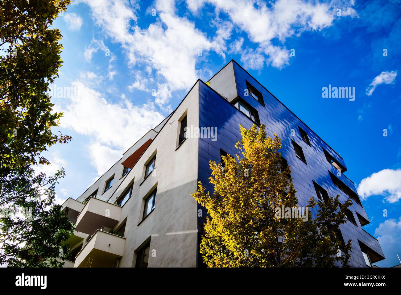 Moderno edificio residenziale con facciata blu riflettente e design geometrico sotto il cielo nuvoloso con luce luminosa Foto Stock