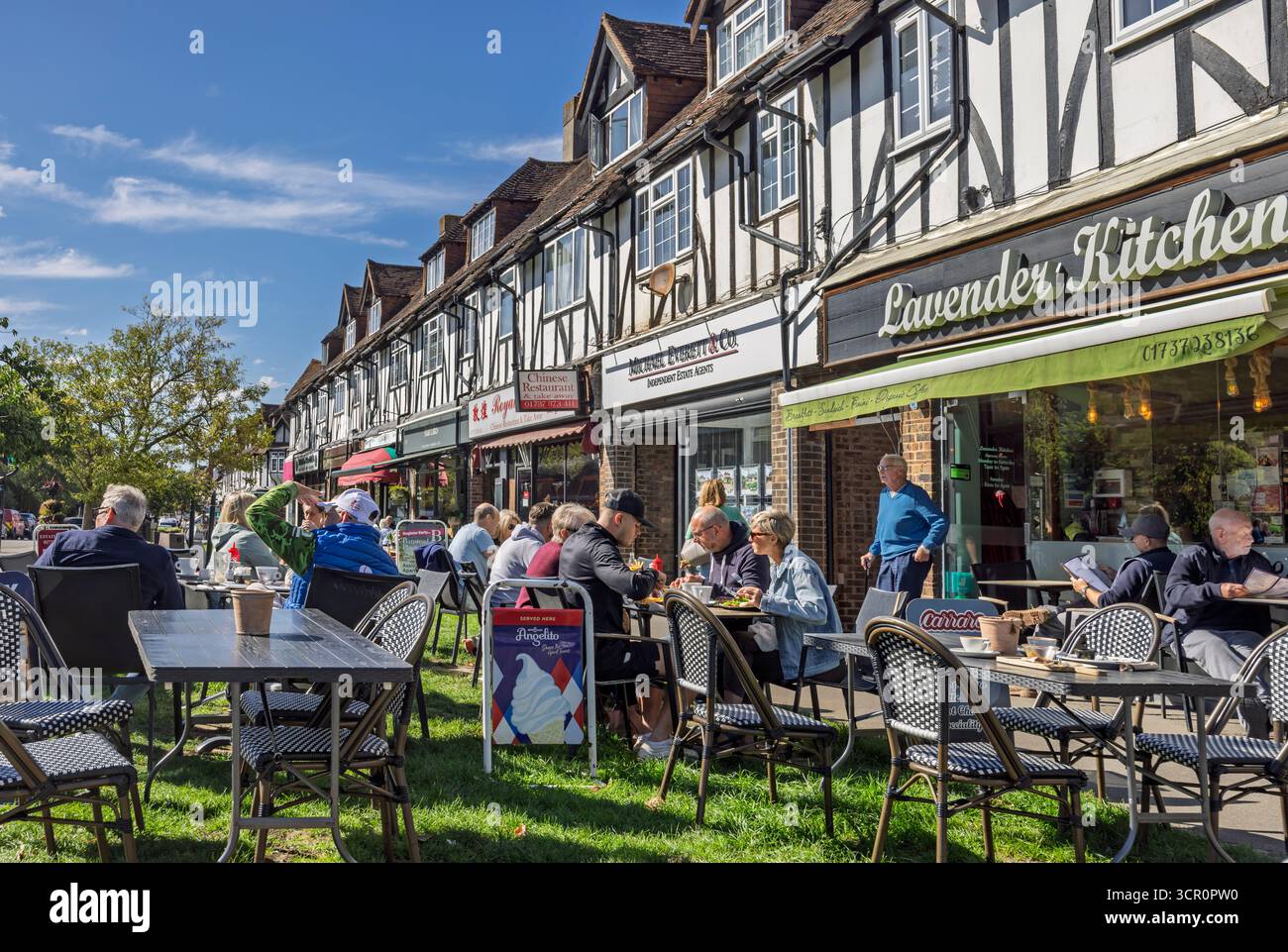 Negozi e caffetterie con posti a sedere all'aperto lungo la verdeggiante High Street a Banstead, Surrey, Regno Unito, il 25 settembre 2025 Foto Stock
