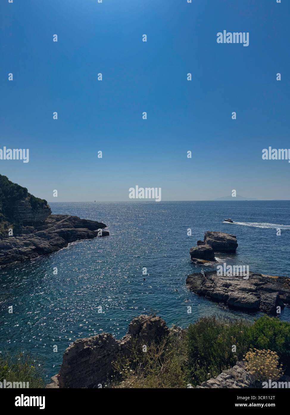 Costa rocciosa con orizzonte blu del mare e luce solare scintillante Foto Stock