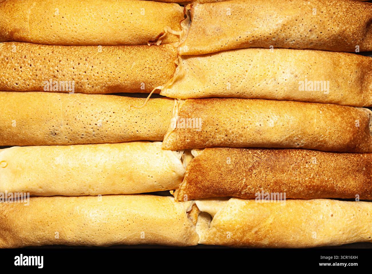 Pancake fritti e arrotolati impilati fianco a fianco su una superficie scura, vista dall'alto, primo piano Foto Stock