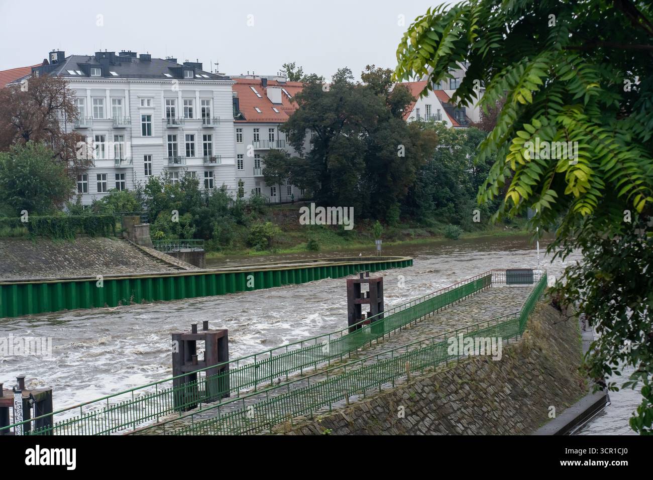 Fiume durante le inondazioni con un rapido flusso vicino al terrapieno e agli edifici residenziali storici. Concetto di impatto ambientale, gestione dell'acqua e affr Foto Stock