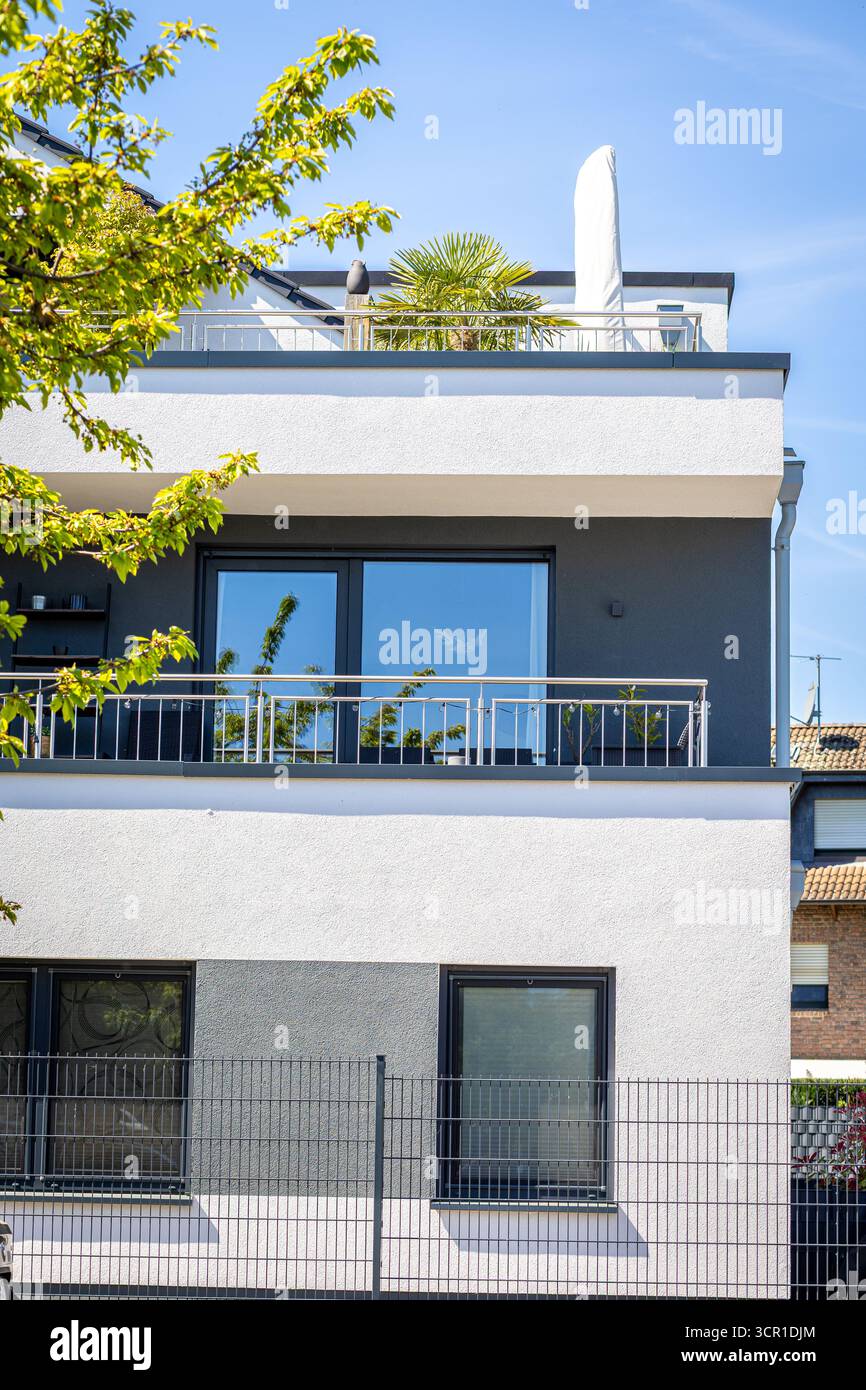 Un elegante edificio di appartamenti presenta un design elegante con grandi finestre e un balcone adornato con piante frondose. Il cielo azzurro e limpido esalta la vibra Foto Stock