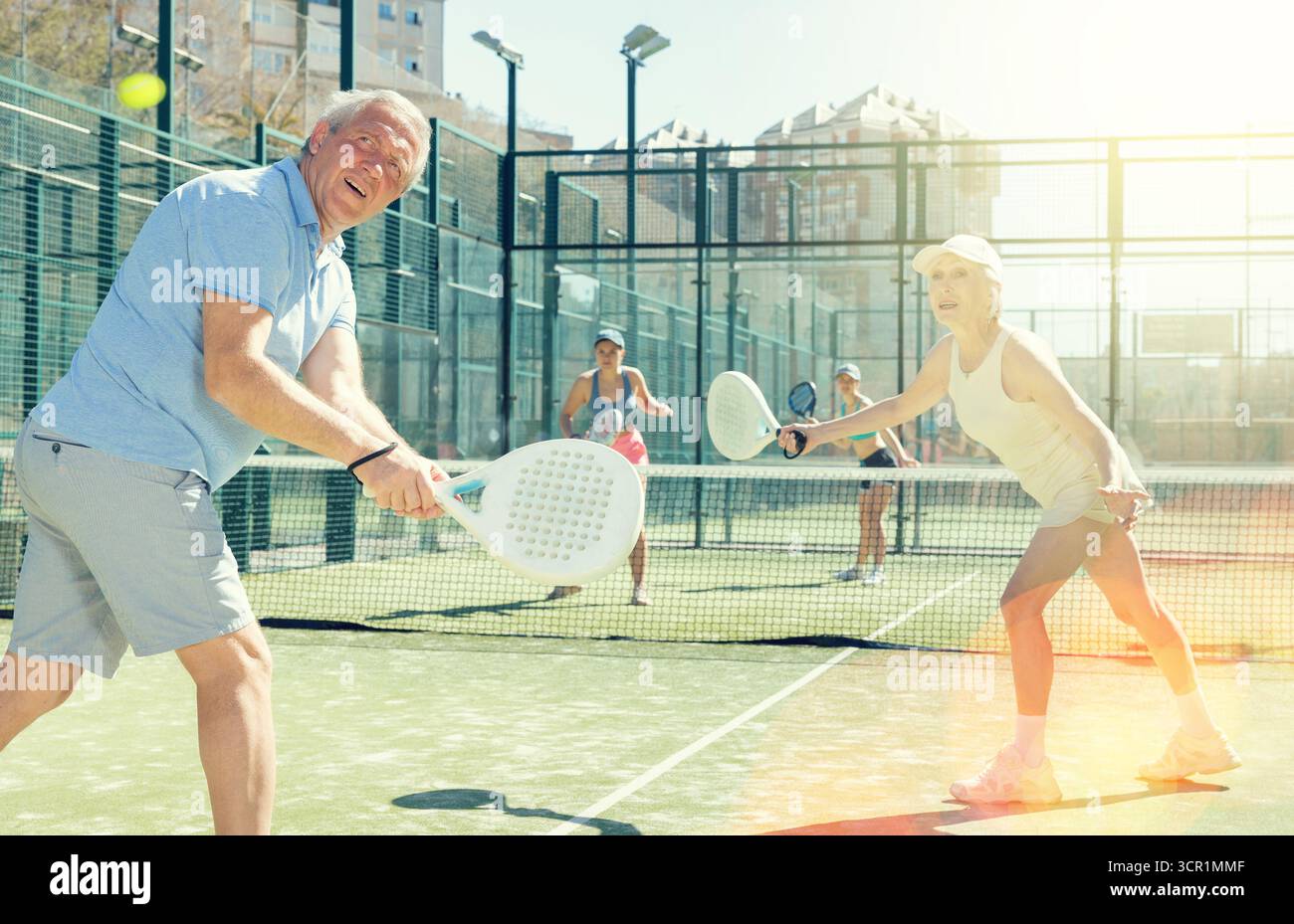 Uomo e donna anziani motivati che giocano a padel con il suo compagno di squadra in tribunale Foto Stock