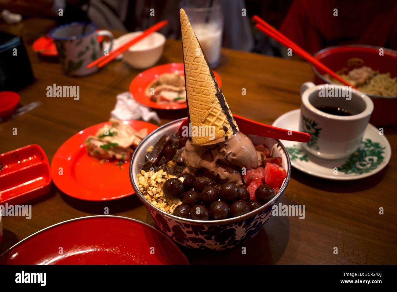 Gelato in una classica ciotola con contorno a cono, palline di cioccolato, noci, budino e anguria, su un tavolo di legno. Foto Stock