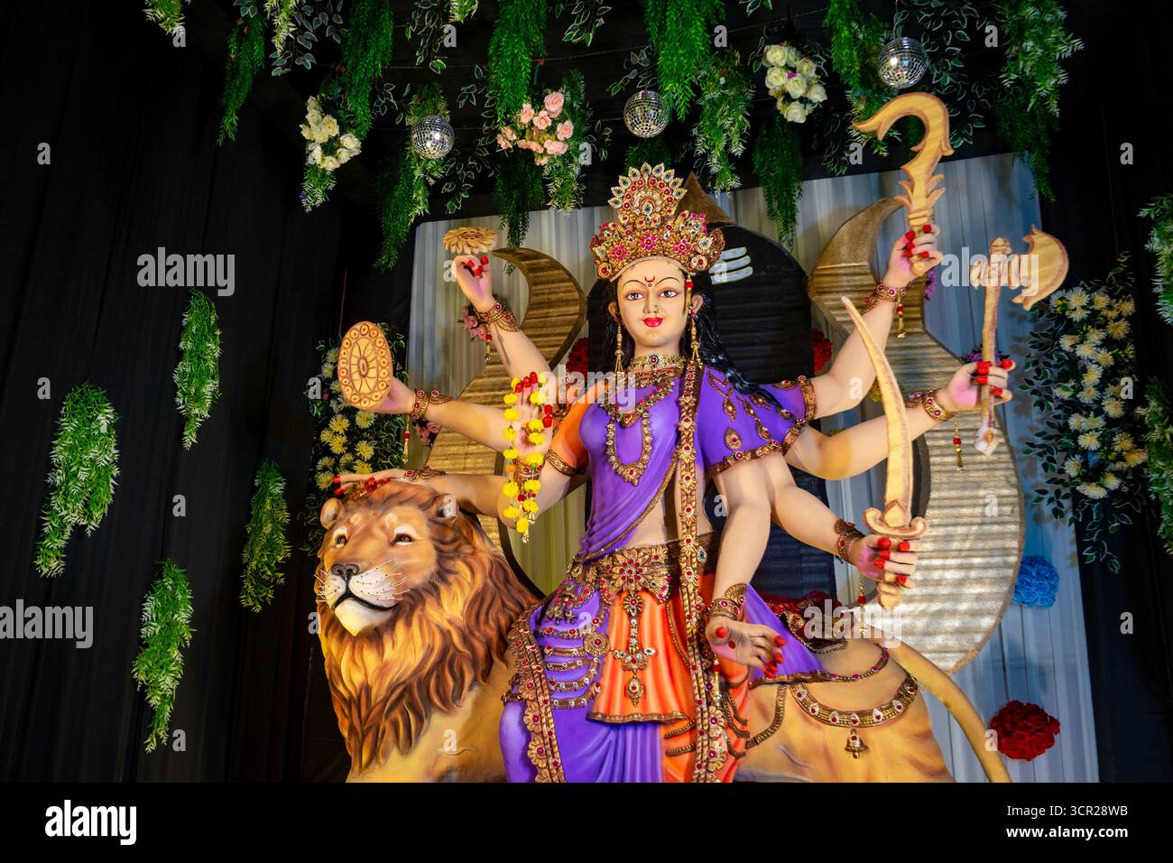 Statua colorata della dea Durga con più braccia in mano armi, seduta su un leone Foto Stock