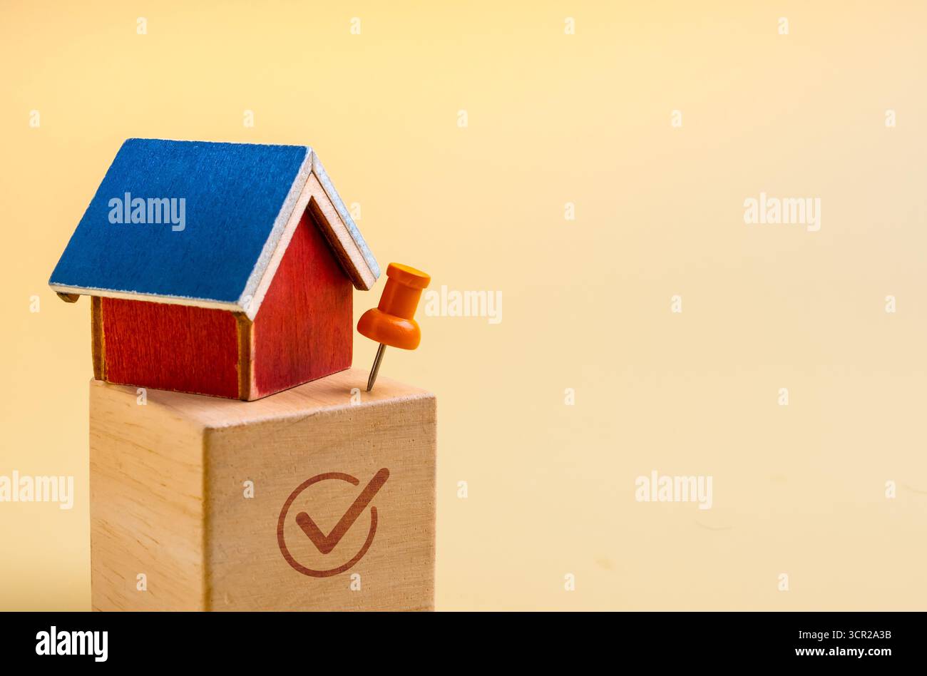Modello mini-House con perno a pressione su blocco di legno e segno di spunta con spazio. Concetto di investimento immobiliare, scelta immobiliare, selezione della posizione Foto Stock