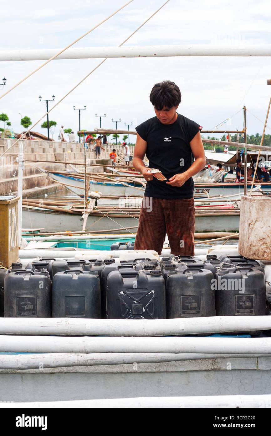 Un uomo che prepara contenitori di plastica per il trasporto in barca usando una banca a Cebu, Filippine Foto Stock