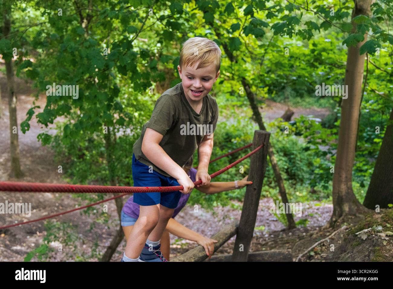 I bambini giocano su scivoli e arrampicate in un parco giochi naturale circondato da alberi. Foto Stock