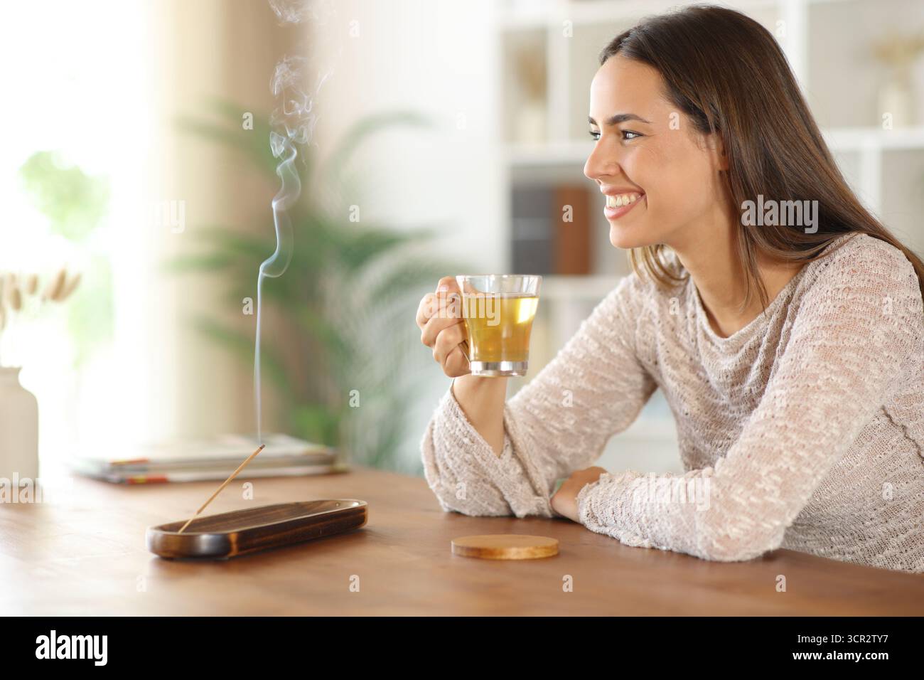 Donna felice che beve un bastoncino di incenso che brucia il tè in una casa che guarda lontano Foto Stock