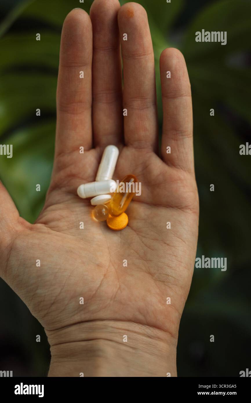 Palmo con vitamine e capsule miste sullo sfondo di piante d'appartamento Foto Stock