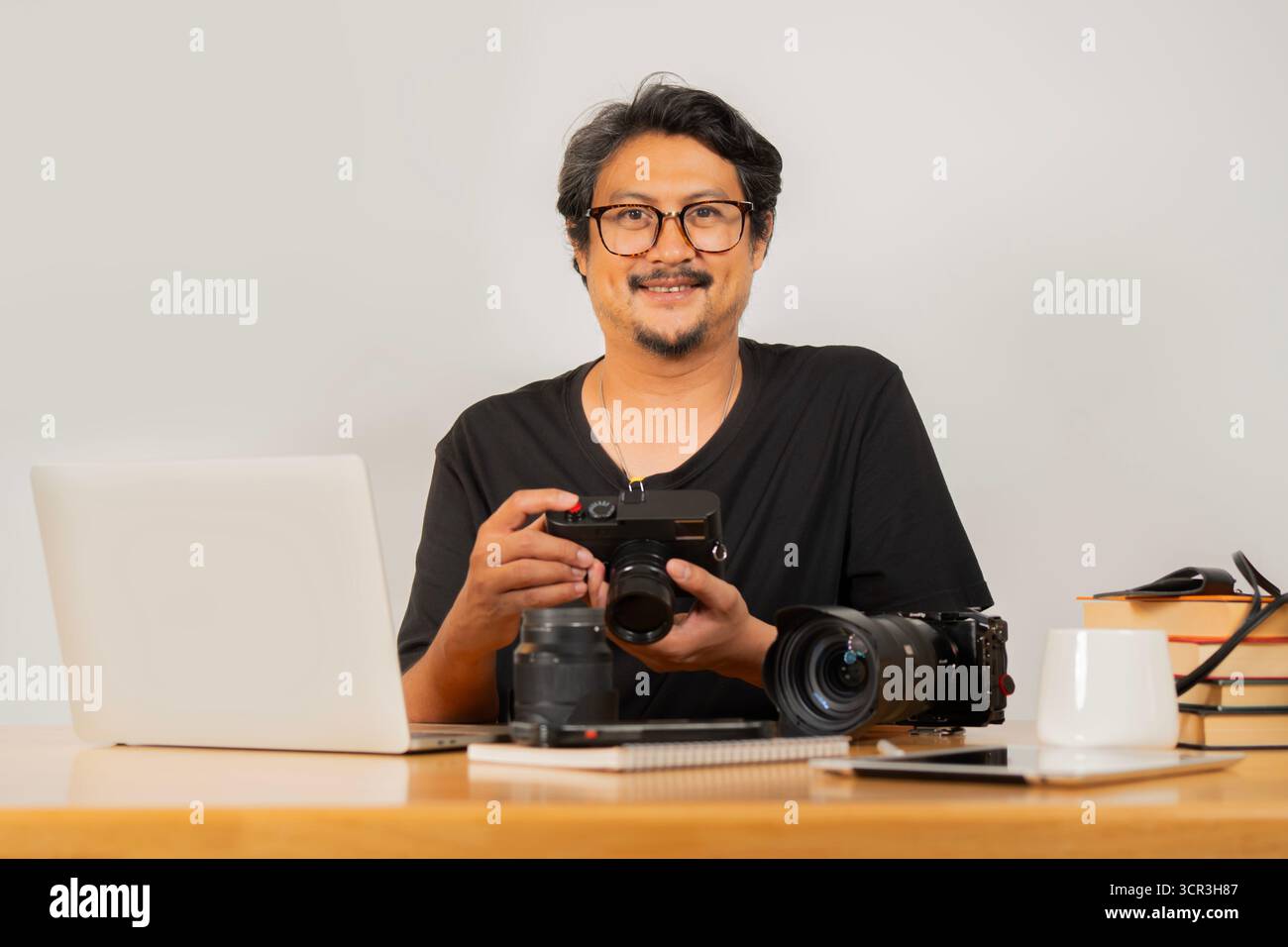 Immagine Protrait di un bellissimo fotografo adulto sorridente con occhiali che lavora con la fotocamera in ufficio. Foto Stock