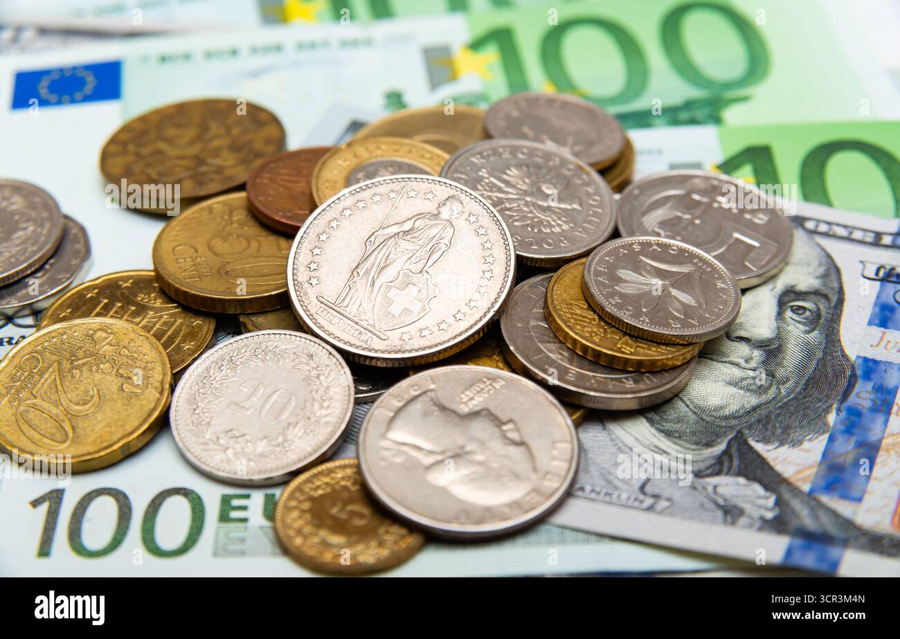 Le monete e le banconote di varie valute riposano insieme, rappresentando il passaggio in corso della finanza verso valute digitali come il bitcoin. Foto Stock