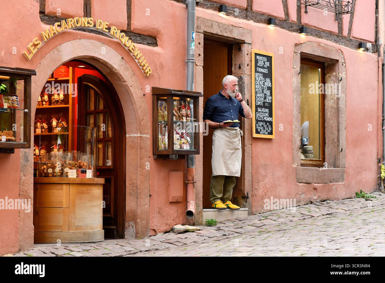 Il negoziante distribuisce assaggi di formaggi locali a Riquewihr sulla strada del vino dell'Alsazia nella Francia orientale. Foto Stock