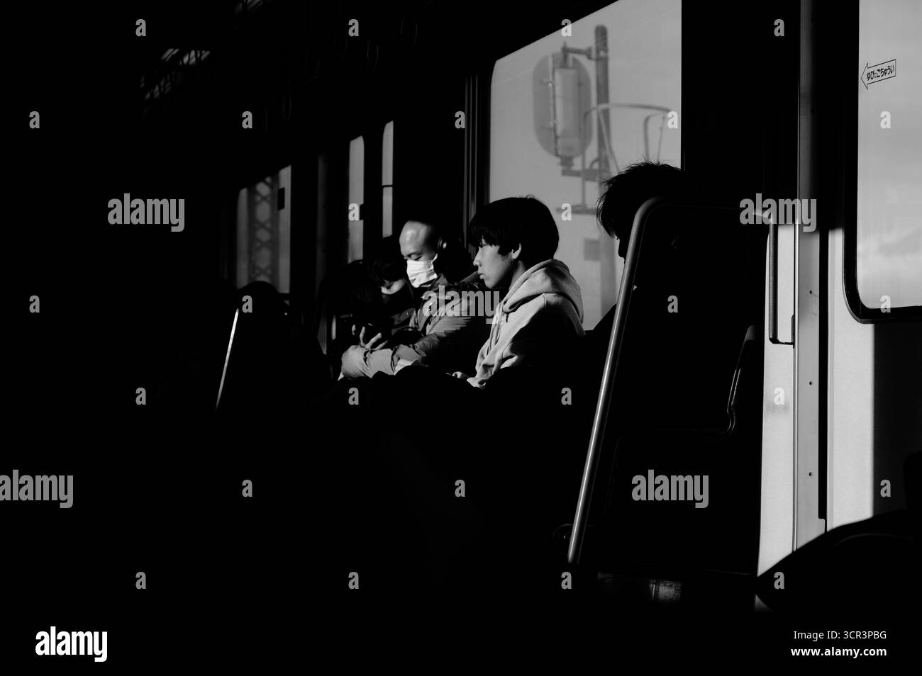 La luce dura taglia il treno a Osaka, isolando i volti in ombra profonda e con un'improvvisa brillantezza Foto Stock