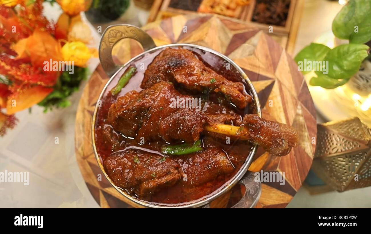 Pollo al curry servito in una teglia al curry, guarnito con foglie di coriandolo fresco. Un tavolo marrone scuro con verdure che ne esaltano il fascino Foto Stock