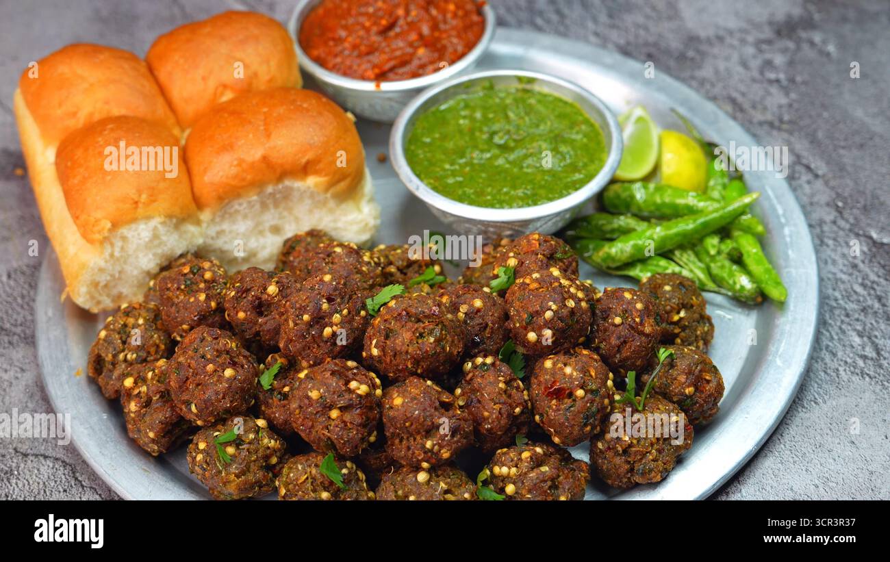 Polpette di kebab con panino servite su un tradizionale piatto di alluminio con chutney rosso e verde, peperoncino verde, limone, pane indiano frizzante, vivaci cibi indiani di strada Foto Stock