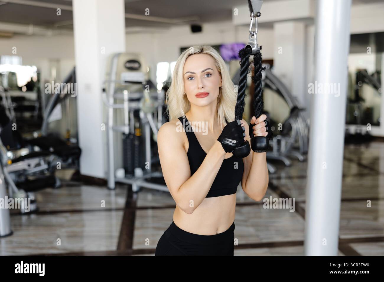 Atleta concentrato che esegue esercizi alla schiena utilizzando una macchina crossover via cavo nel moderno centro fitness, concentrandosi sulla costruzione della forza e sulla definizione dei muscoli Foto Stock