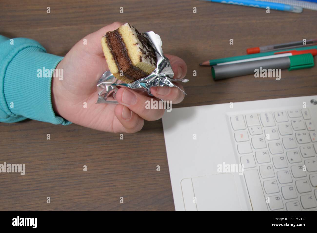 Consumo eccessivo di dolci per i bambini. Adolescente con una torta mentre studiava al computer. Foto Stock