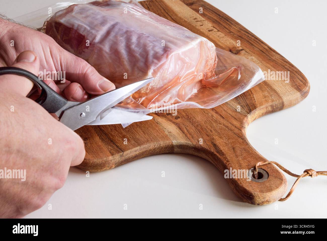 Un uomo taglia un pacchetto sottovuoto con un pezzo di carne con forbici da cucina. Primo piano Foto Stock