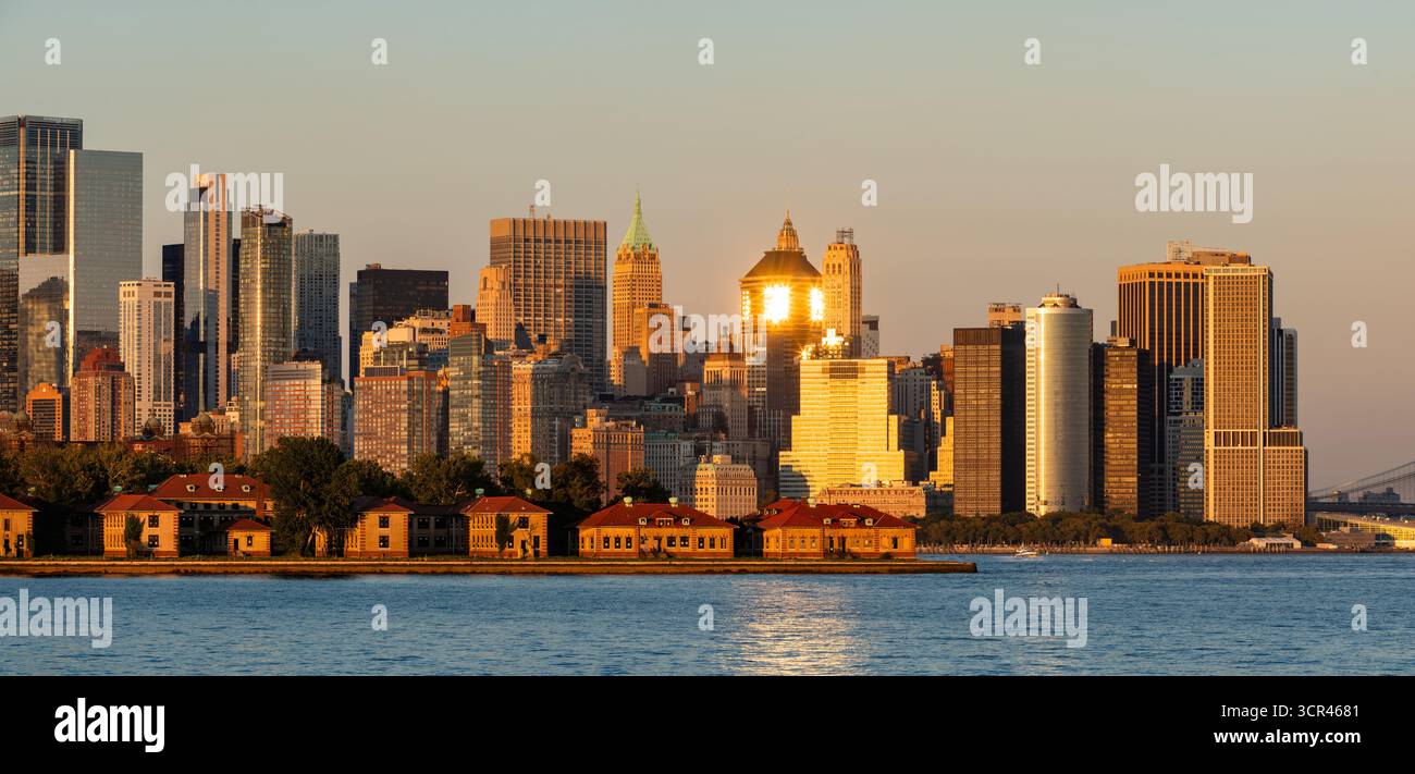 Vista della città di New York dello skyline di Lower Manhattan al tramonto con i grattacieli del Financial District. Ellis Island edifici storici in primo piano Foto Stock