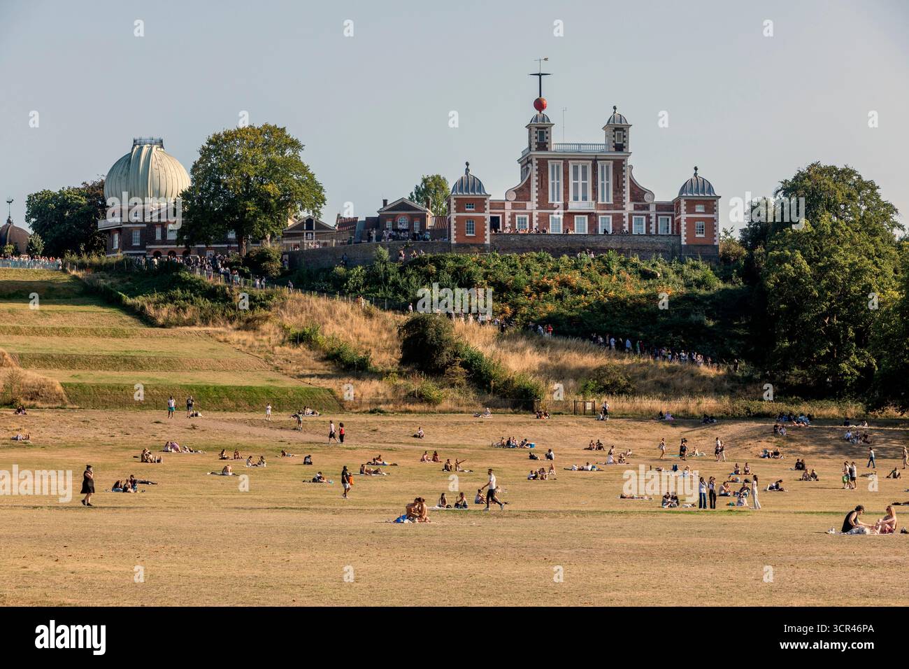 Persone che si rilassano su una collina erbosa vicino all'Osservatorio reale sotto un cielo azzurro. Greenwich Park, Londra, Regno Unito Foto Stock