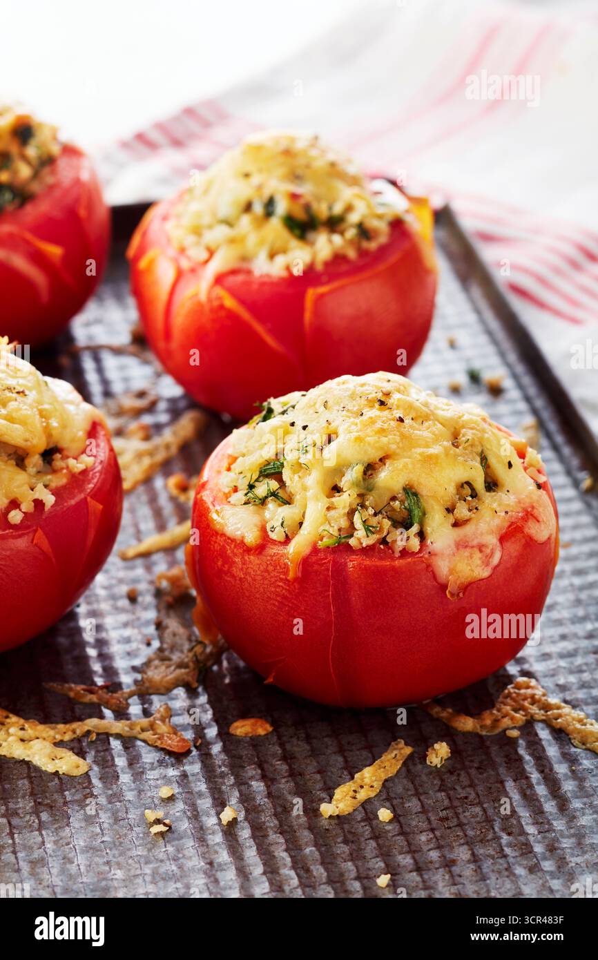 Pomodori ripieni appena sfornati ripieni di erbe e ricoperti di formaggio fuso su un vassoio Foto Stock