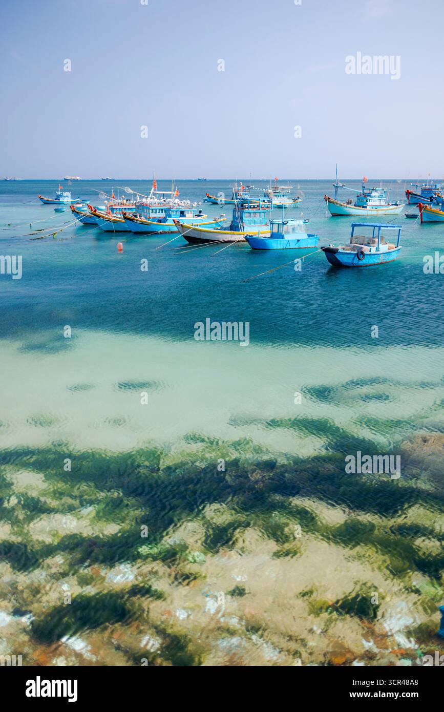 Colorate barche da pesca ancorate in acque turchesi cristalline in una giornata di sole lungo la costa. Isola di Phu Quy, B‐ nh Thuan, Vietnam Foto Stock