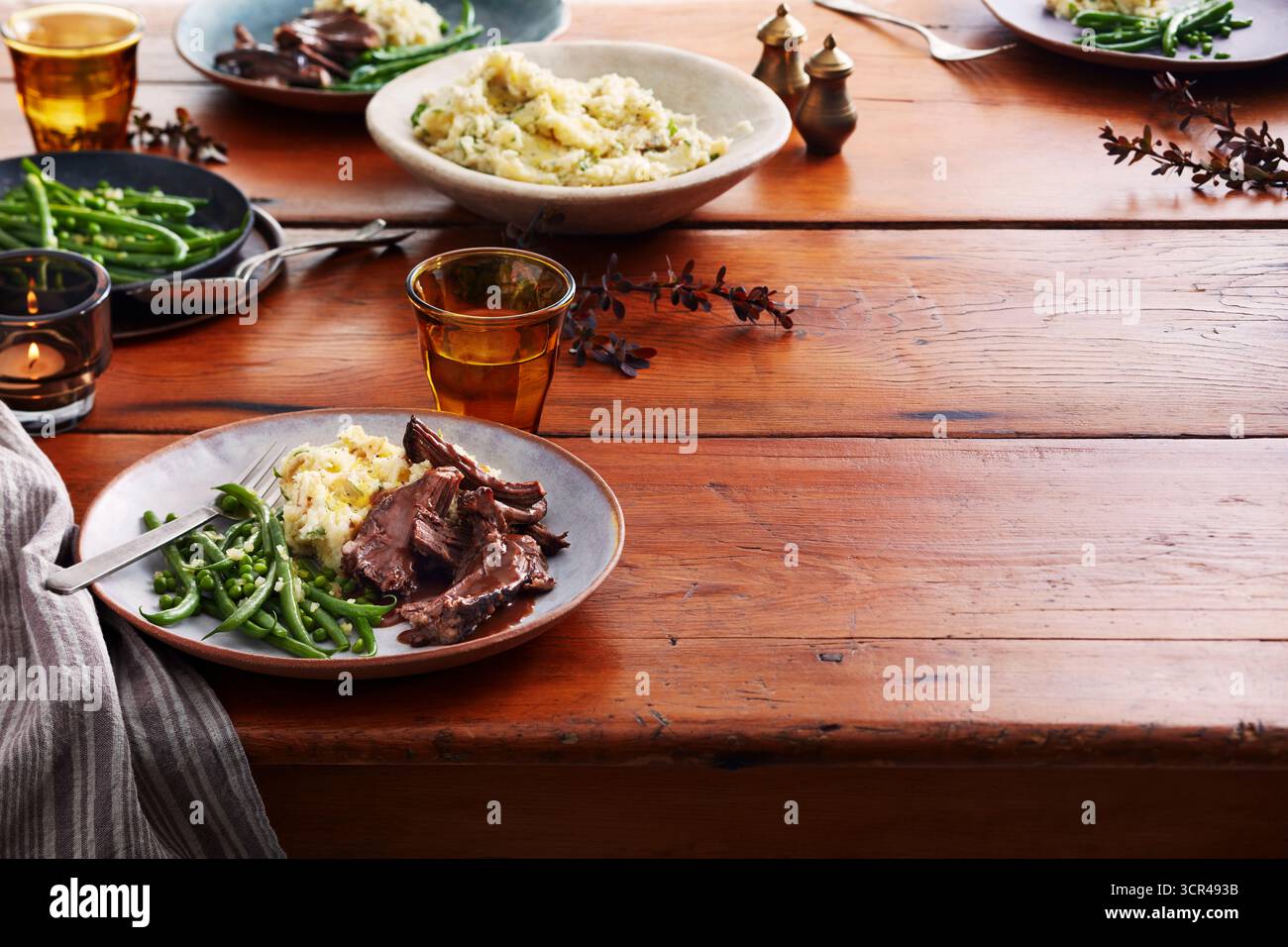 Tavolo con piatti di manzo, fagiolini, purè di patate e bevande su un tavolo di legno. Foto Stock