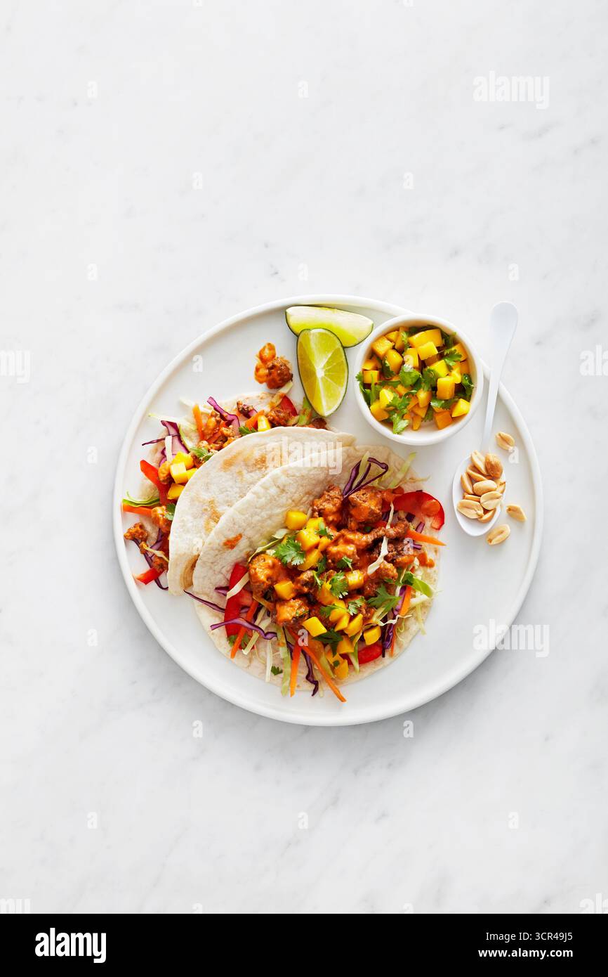 Tacos freschi con un lato di salsa di mango e spicchi di lime su un piatto bianco. Foto Stock