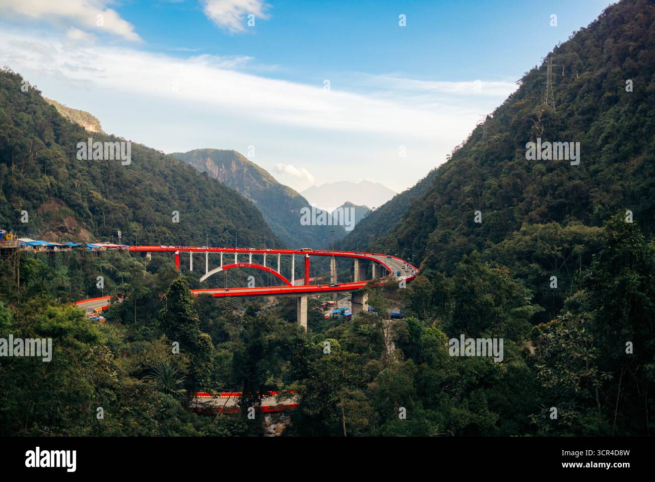 Un ponte rosso vibrante serpeggia attraverso lussureggianti montagne verdi sotto un cielo azzurro. Kelok 9, o i 9 tornanti, Harau, West Sumatra, Indonesia Foto Stock