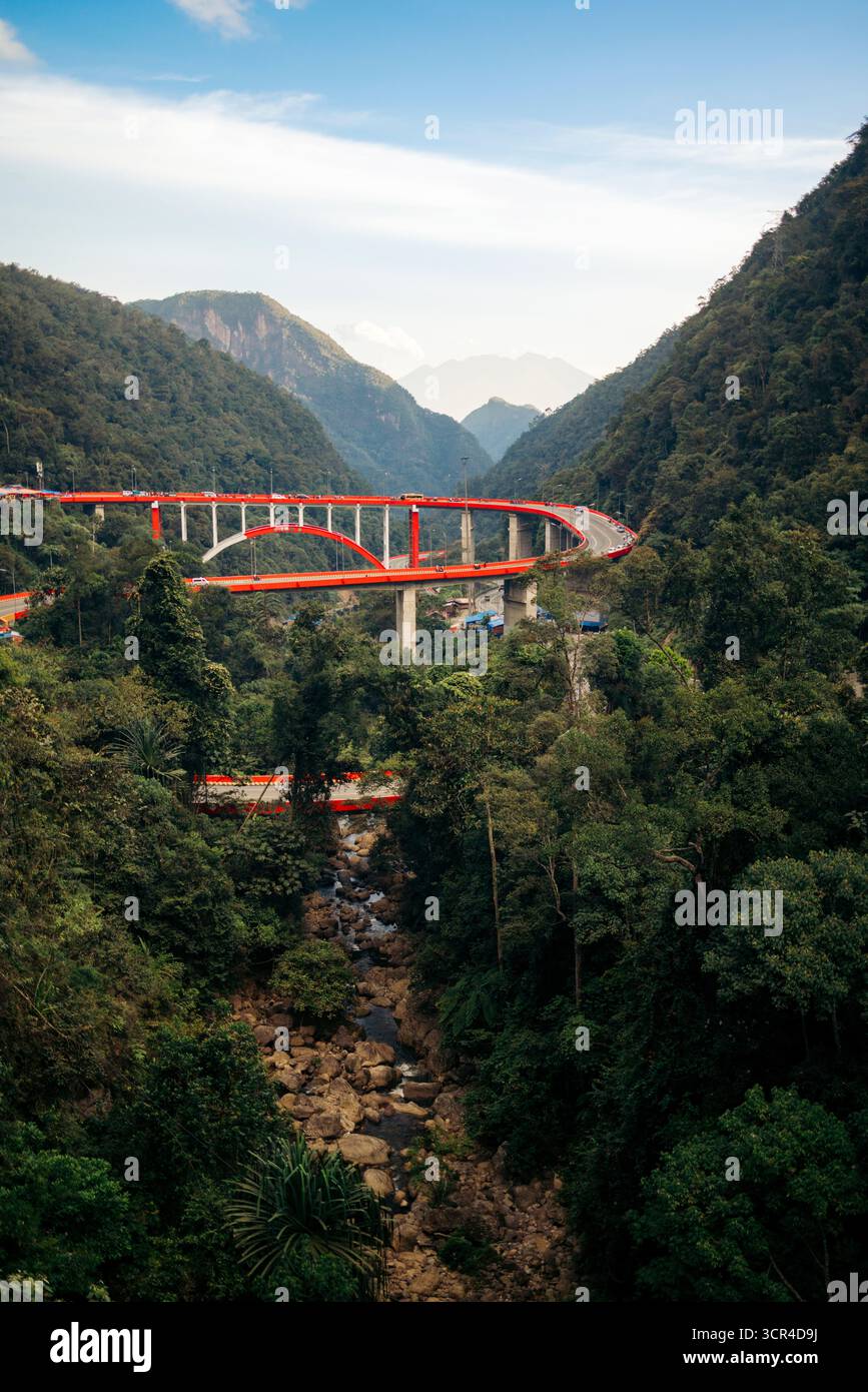 Il ponte rosso si snoda attraverso lussureggianti montagne verdi sotto un cielo azzurro. Kelok 9, o i 9 tornanti, Harau, West Sumatra, Indonesia Foto Stock