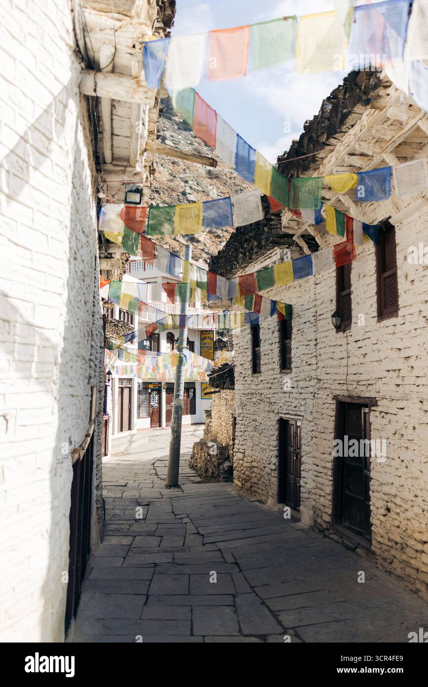 Stretto vicolo in pietra in un villaggio rustico adornato da colorate bandiere di preghiera. Marpha, Annapurna, distretto di Mustang della provincia di Gandaki, Nepal Foto Stock
