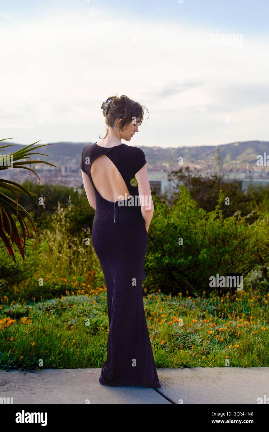Donna con un abito nero si erge all'aperto con colline sullo sfondo. Foto Stock