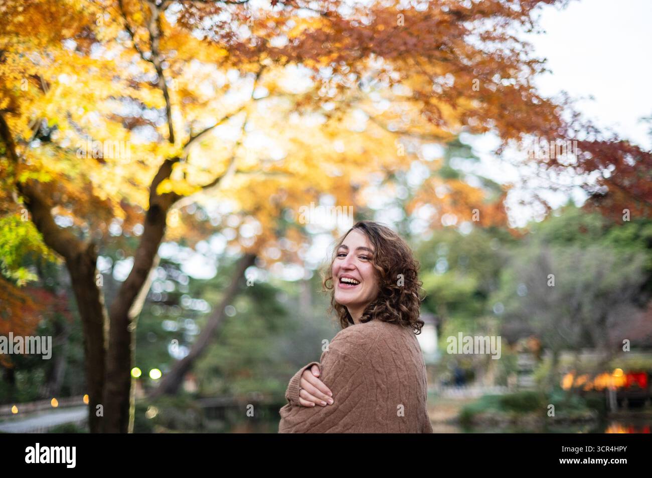Donna che ride nella foresta autunnale indossa un comodo pullover Foto Stock