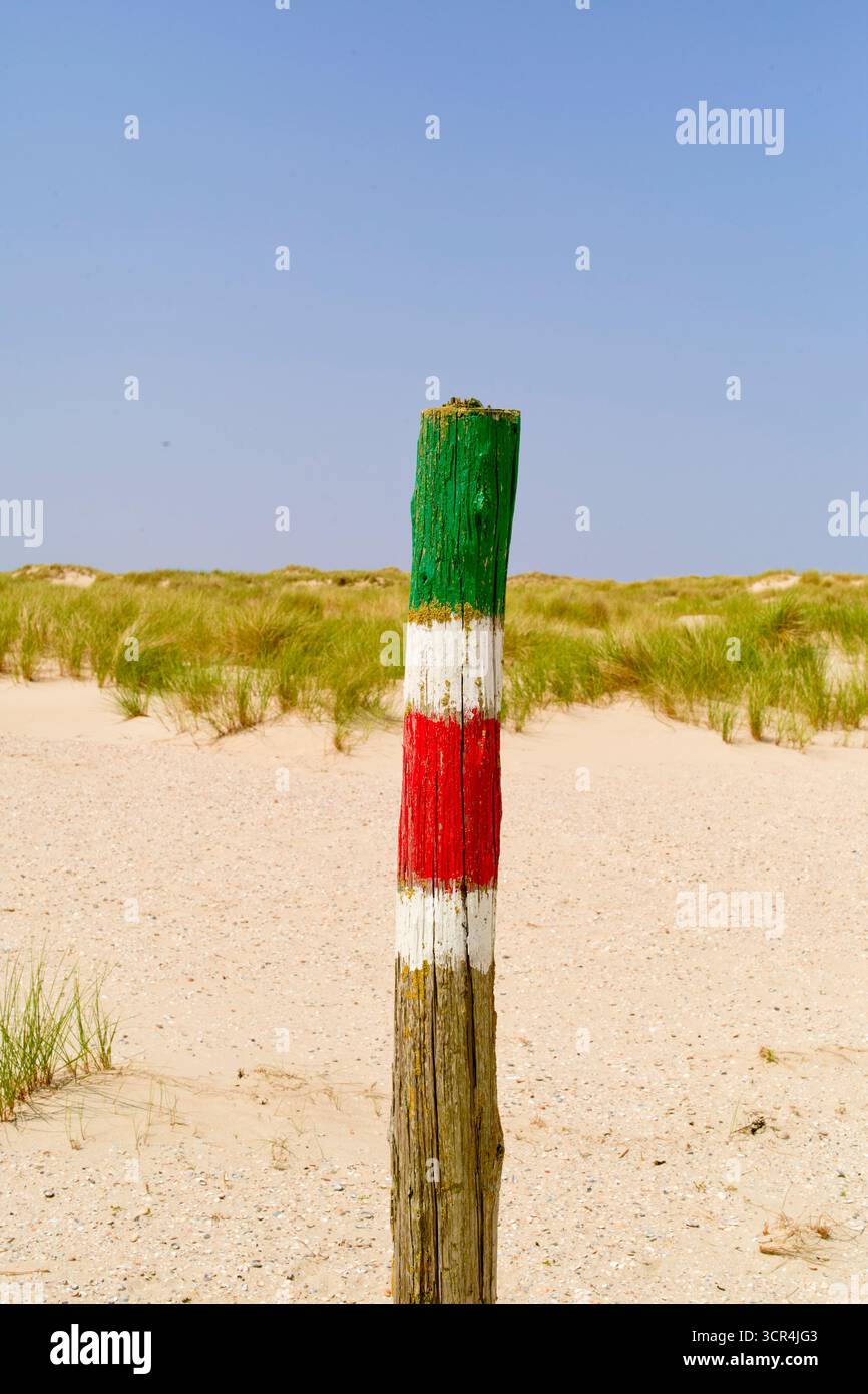 Palo in legno su una spiaggia di sabbia dipinta di verde, bianco e rosso contro una duna erbosa. Mare del Nord, Germania Foto Stock