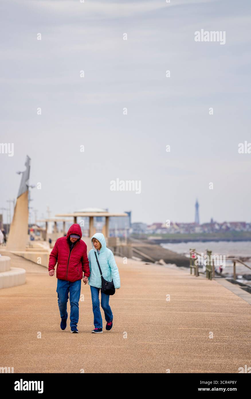 Un uomo e una donna più anziani camminano mano nella mano lungo il lungomare di Cleveleys, Lancashire, Regno Unito Foto Stock