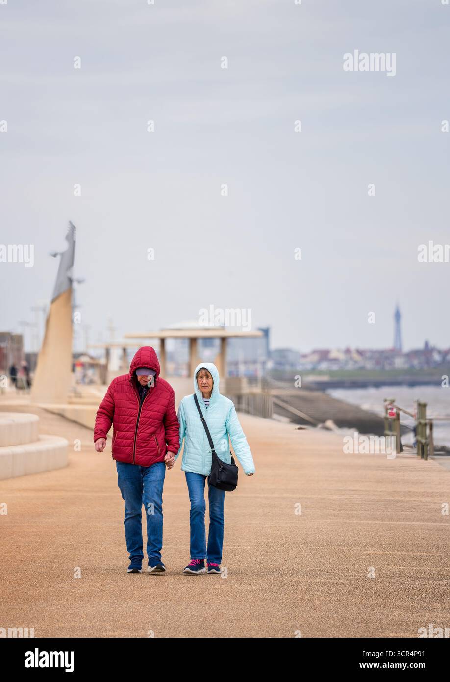 Un uomo e una donna più anziani camminano mano nella mano lungo il lungomare di Cleveleys, Lancashire, Regno Unito Foto Stock