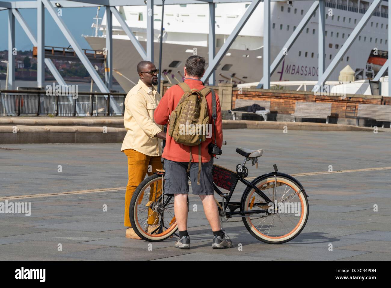 Due uomini, uno nero e uno bianco con una bicicletta, chiacchierano sul lungomare di Albert Dock, Liverpool, Regno Unito Foto Stock