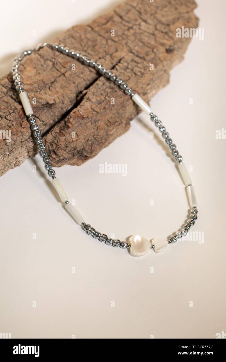 Una splendida collana di bigiotteria poggia su un pezzo di legno testurizzato. Presenta perle argentate e dettagli bianchi che creano un'atmosfera elegante e accattivante Foto Stock