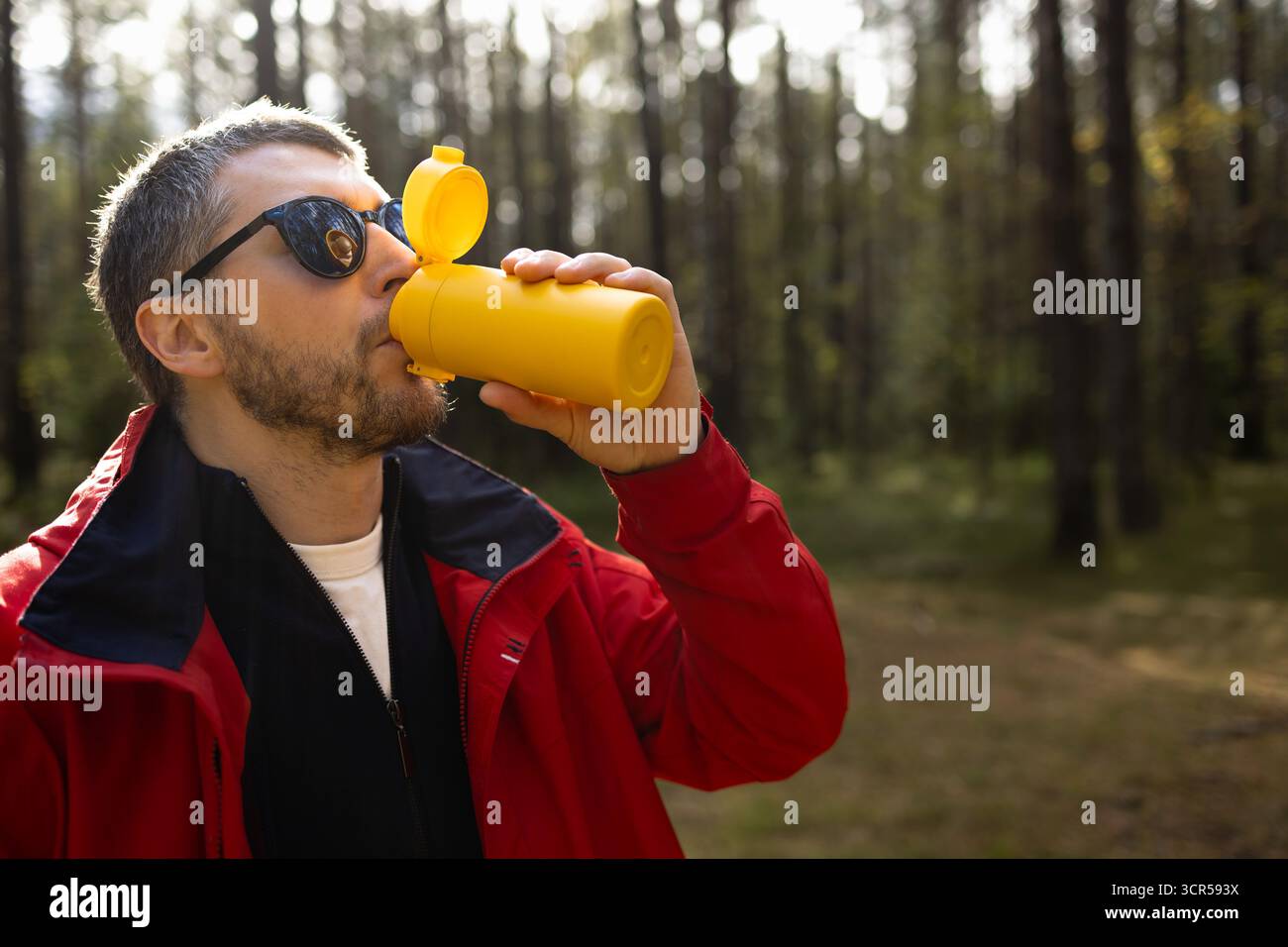 Uomo che si gode una bevanda calda da una tazza da viaggio riutilizzabile mentre si trova in mezzo alla natura. Perfetto per temi di stile di vita ecologico, viaggi all'aperto e vita sana Foto Stock