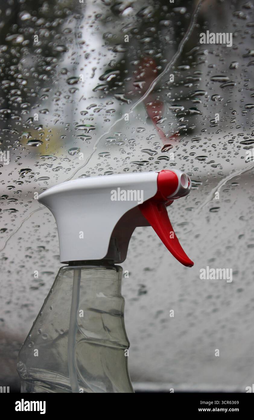 Un flacone spray di detergente per vetri vicino a una finestra bagnata dalla pioggia. Foto di scorta per pulizia domestica e protezione finestre Foto Stock
