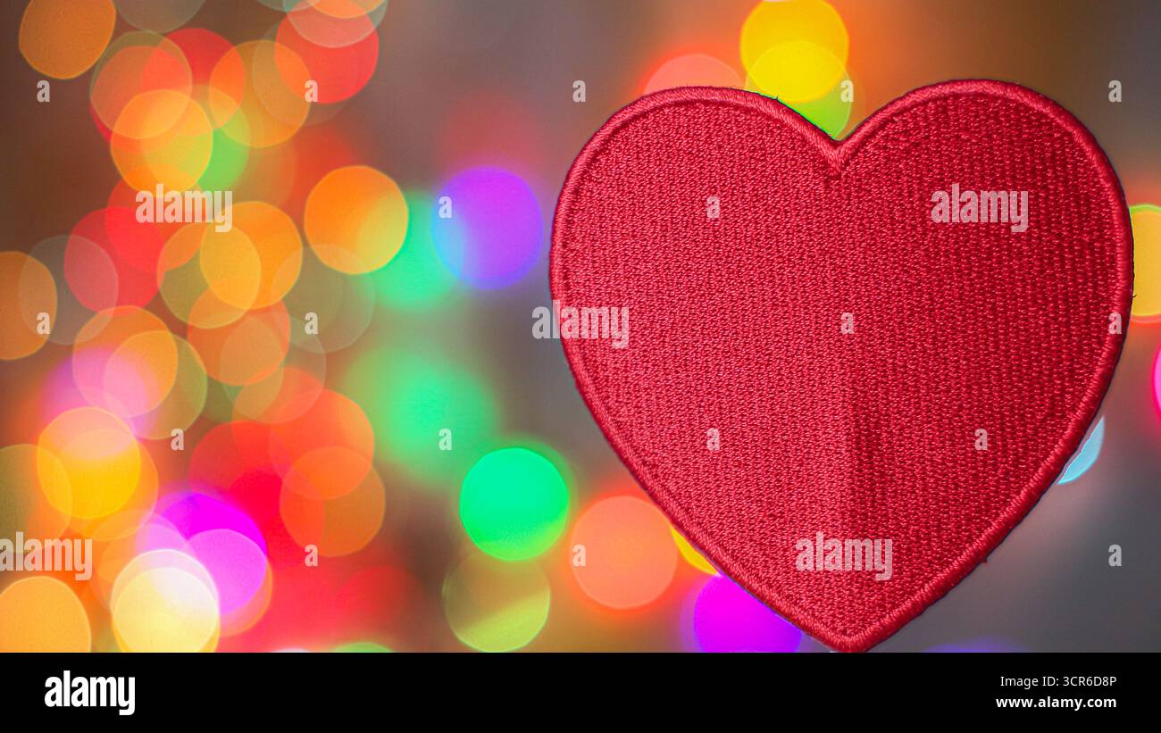 Cuore ricamato rosso su morbido sfondo bokeh colorato con spazio per copie, tema romantico per San Valentino o design per matrimoni. Foto Stock