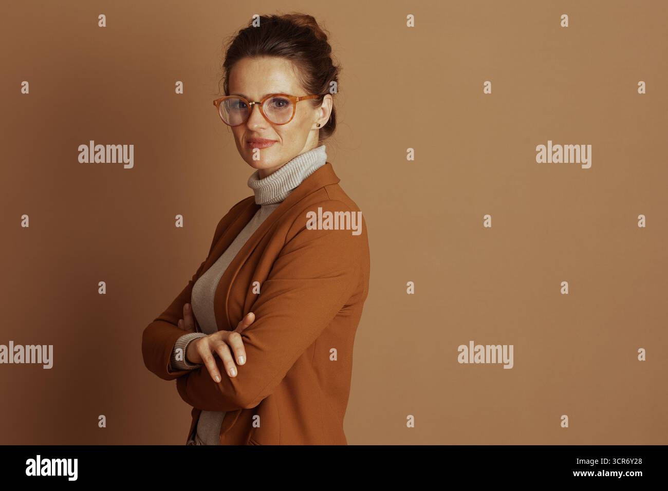 Un professionista di mezza età con occhiali con cornice arancione e un sorriso sottile si staglia con le braccia incrociate, incarnando intelligenza, competenza e un moderno, co Foto Stock