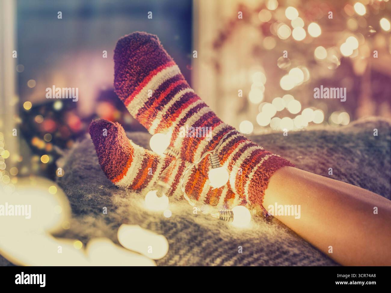 piedi in calze a righe e luci fatate sul divano Foto Stock