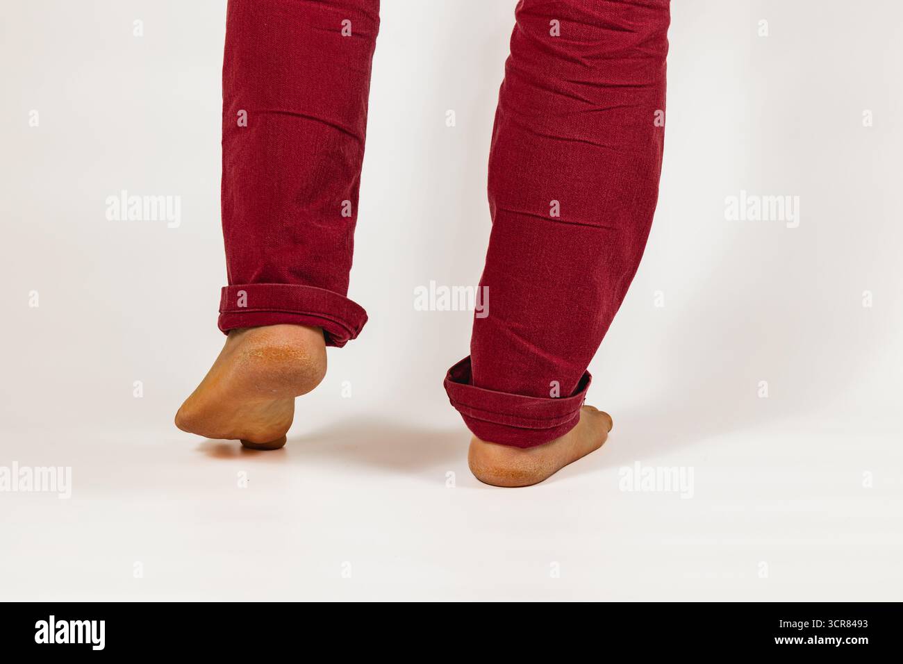 Una persona si sta bilanciando sulle dita dei piedi indossando pantaloni rossi arrotolati. L'attenzione è concentrata sui loro piedi con uno sfondo neutro, che trasmette un gioco giocoso e leggero Foto Stock