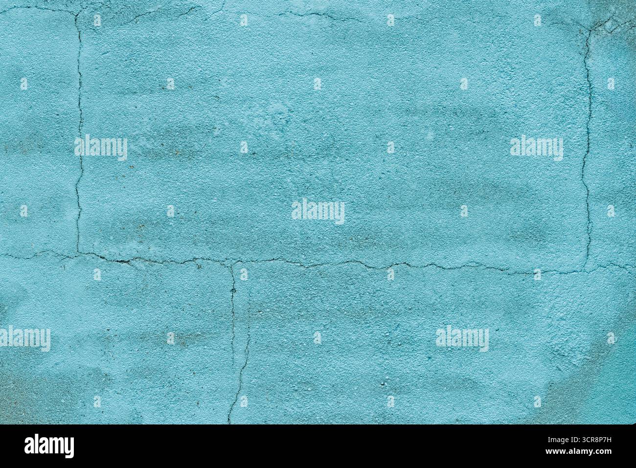 Superficie di una parete turchese che mostra crepe e una consistenza ruvida sotto la luce solare intensa, aumentando l'interesse visivo dell'ambiente. Foto Stock